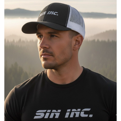 Man wearing a street wear trucker hat from Sin Inc. against a mountain backdrop, showcasing edgy vixen style street wear trucker hats.